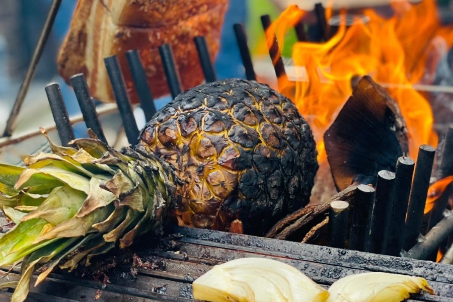 eine Ananas und Fleisch grillen im Feuer auf einem handgefertigten Grill von Münz – Die Manufaktur