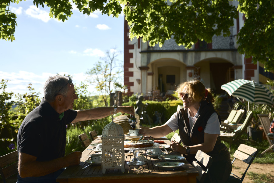 Mann und Frau sitzen an einem gedeckten Tisch auf der schattigen Terrasse vor der Burg Gamburg